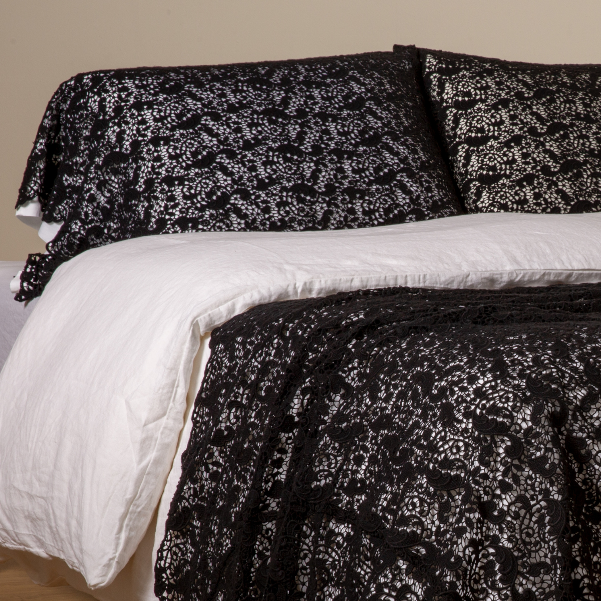 Corvino Allora Lace pillowcases on bed, black lace-patterned fabric with white linen beneath.