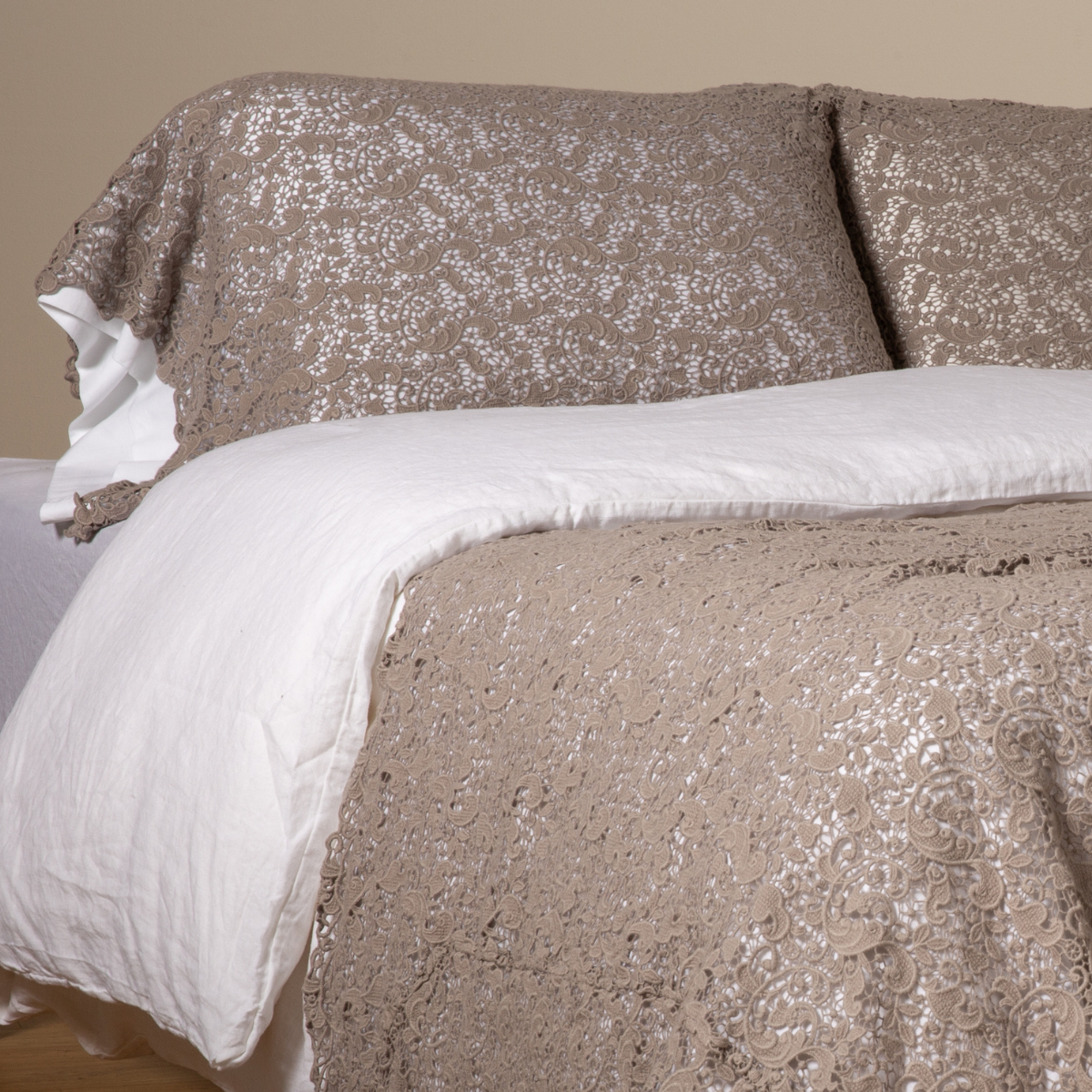 Fog lace pillowcase and duvet styled on bed with white linen layers, close angled view.