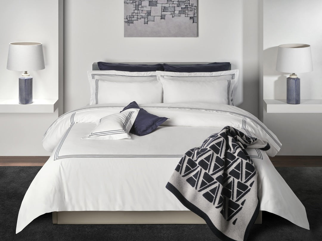 Full bedroom styled with white Alvorada bedding, navy accents, and geometric throw.