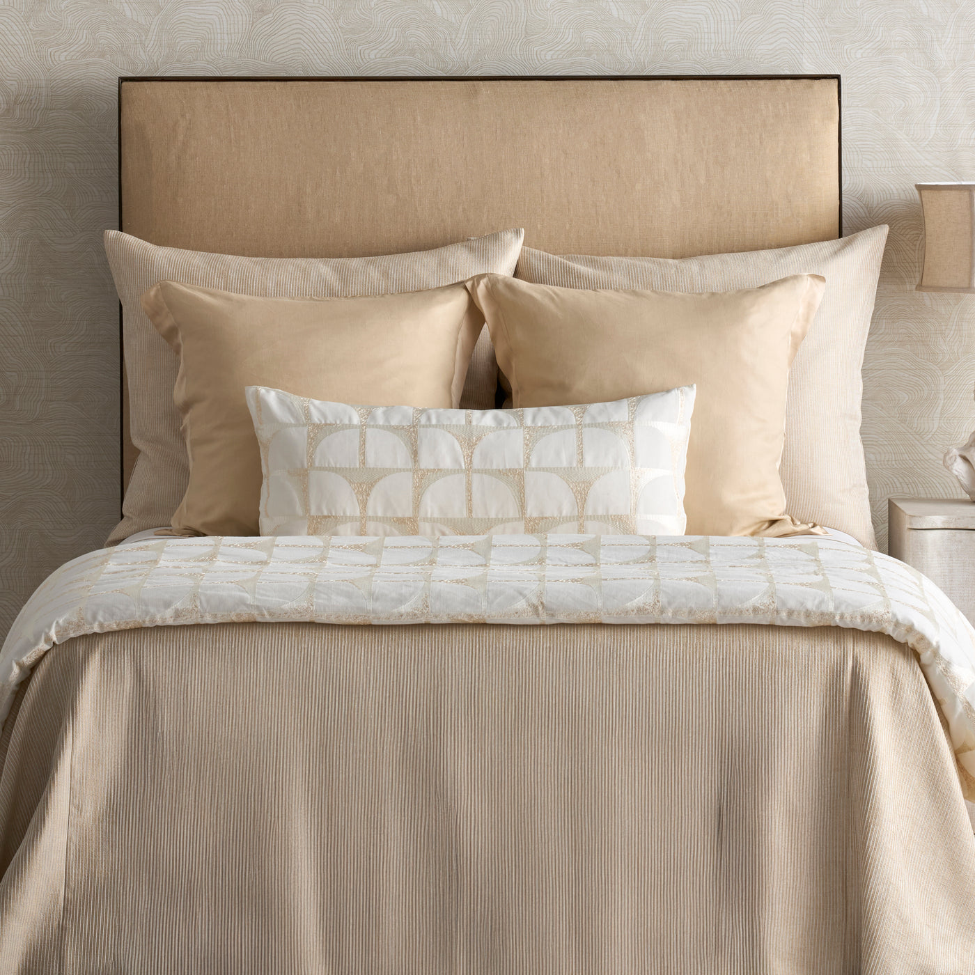White lumbar pillow with champagne arch embroidery, styled on a neutral linen bed.