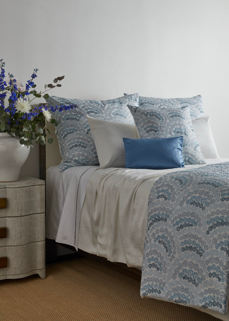 Close-up of Ann Gish Asperitas coverlet in blue-teal scalloped pattern on styled bed.