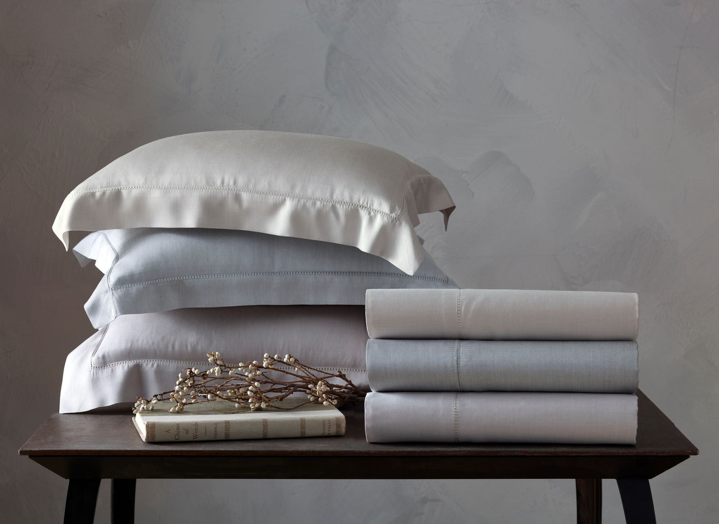 Close-up of folded Home Treasures Atwood sheets in white and pale blue on a wood table.