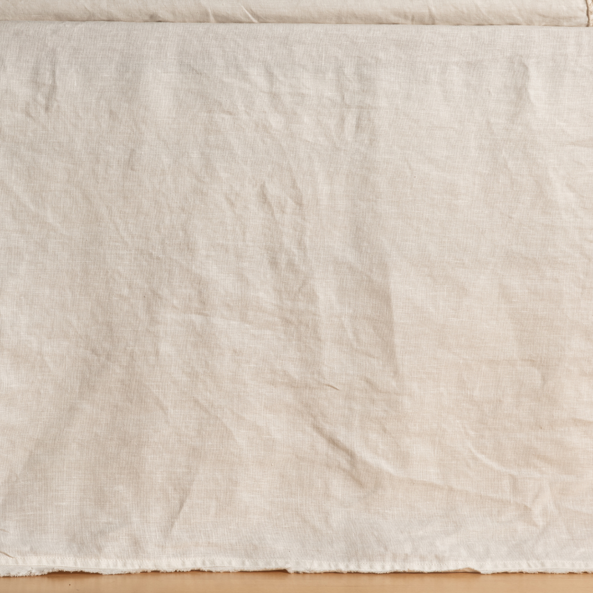 Bella Notte Austin bed skirt in Natural, showing relaxed linen drape and raw hem detail.