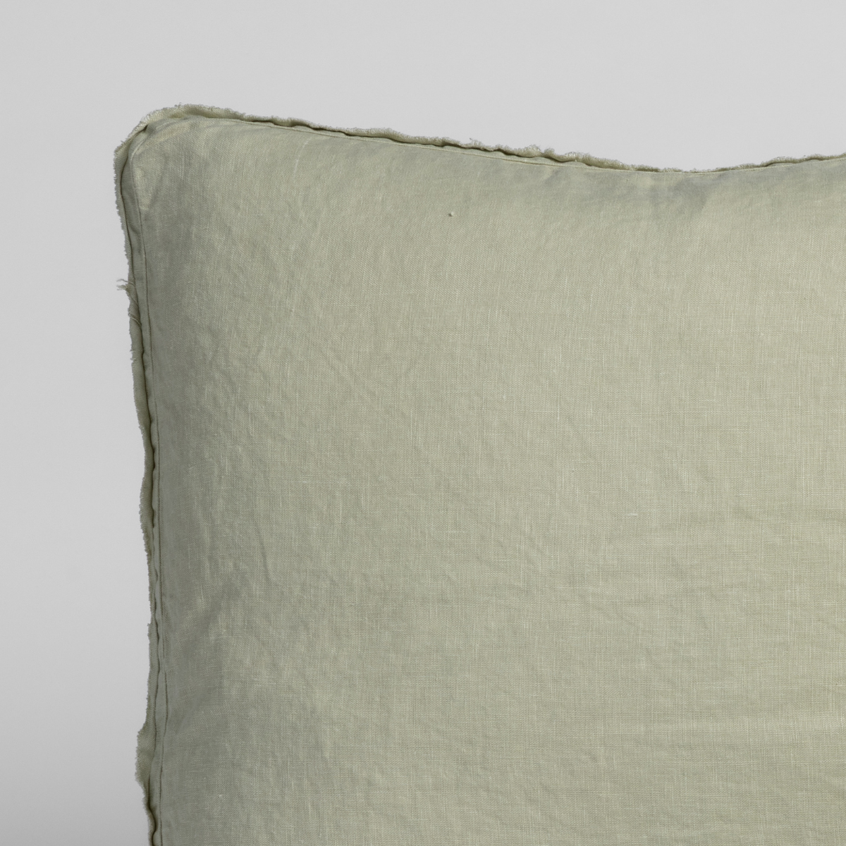 Close-up corner detail of Desert Sage linen sham with raw frayed edge trim.