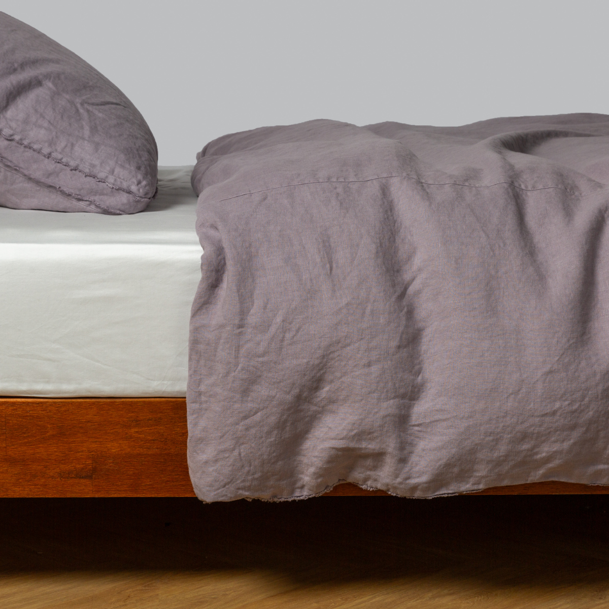 Casually draped French Lavender linen duvet cover on a low wood-frame bed.