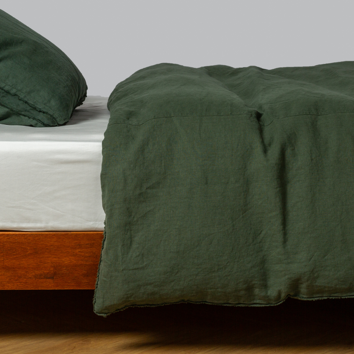 Deep Juniper linen duvet cover draped over bed corner, showing relaxed texture and natural drape.