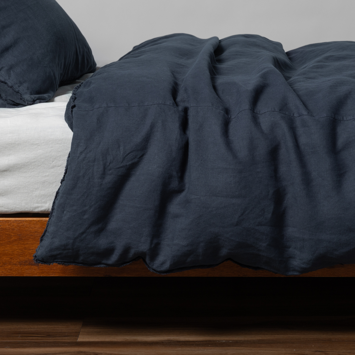 Draped slate linen duvet cover on a low wood-frame bed, casually rumpled.