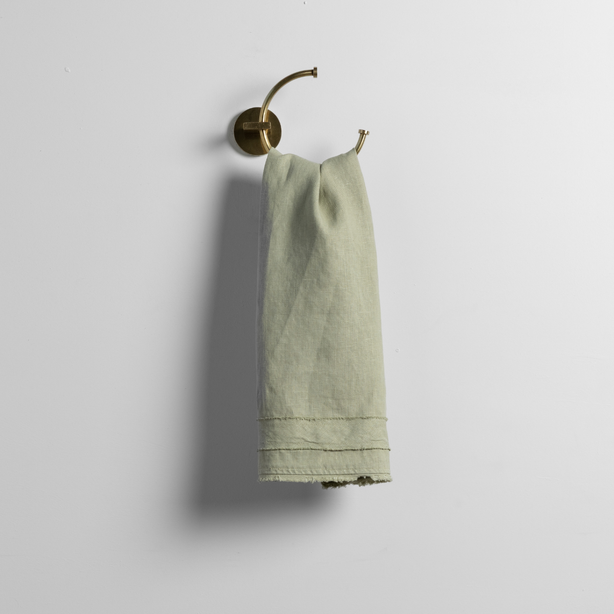 Desert Sage guest towel hanging from brass ring hook, showing hem detail and frayed edge.