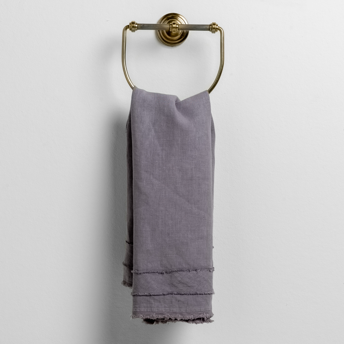 Frayed hem detail on French Lavender linen guest towel draped over brass ring.