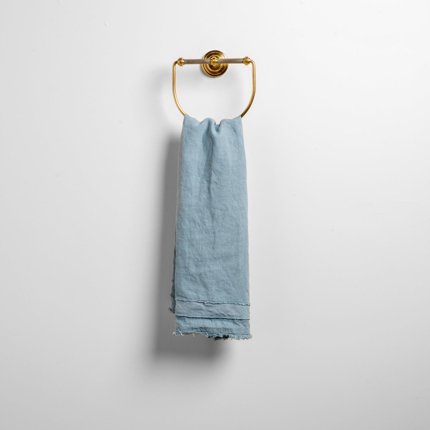 Tahoe Blue linen guest towel draped over a brass ring on a white wall.