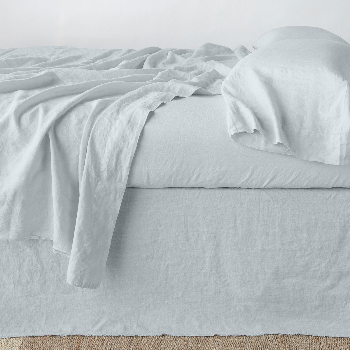 Bella Notte Austin bed skirt in Cloud, shown with matching linen flat sheet draped casually over bed.