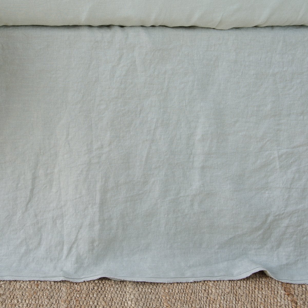Bella Notte Austin bed skirt in Eucalyptus, relaxed linen drape pooling above woven rug.