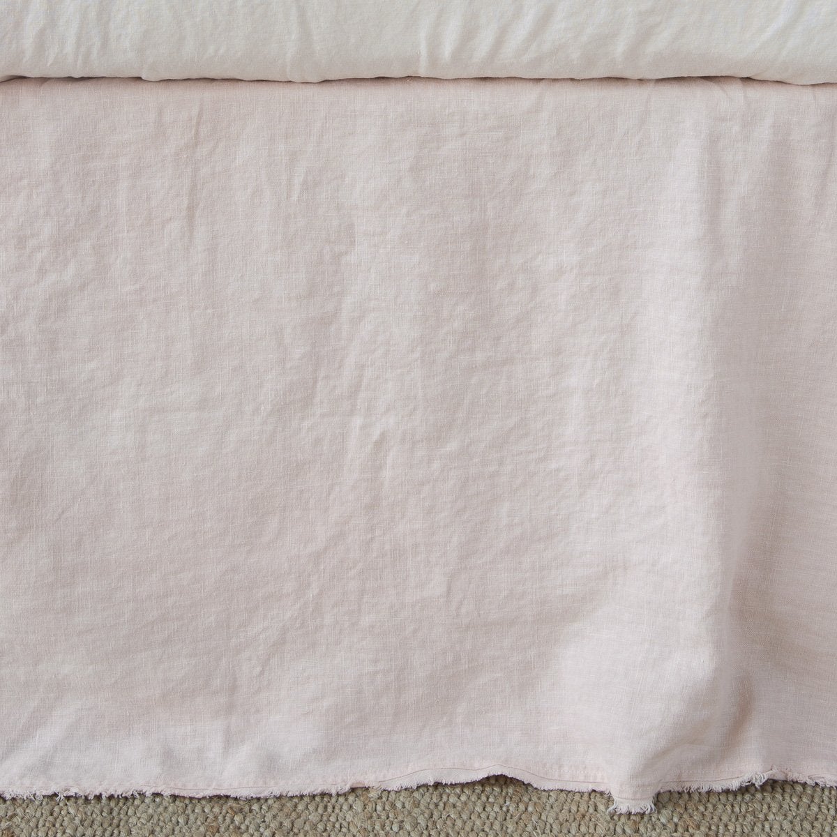 Bella Notte Austin bed skirt in Pearl, showing relaxed linen drape with raw fringe hem detail.