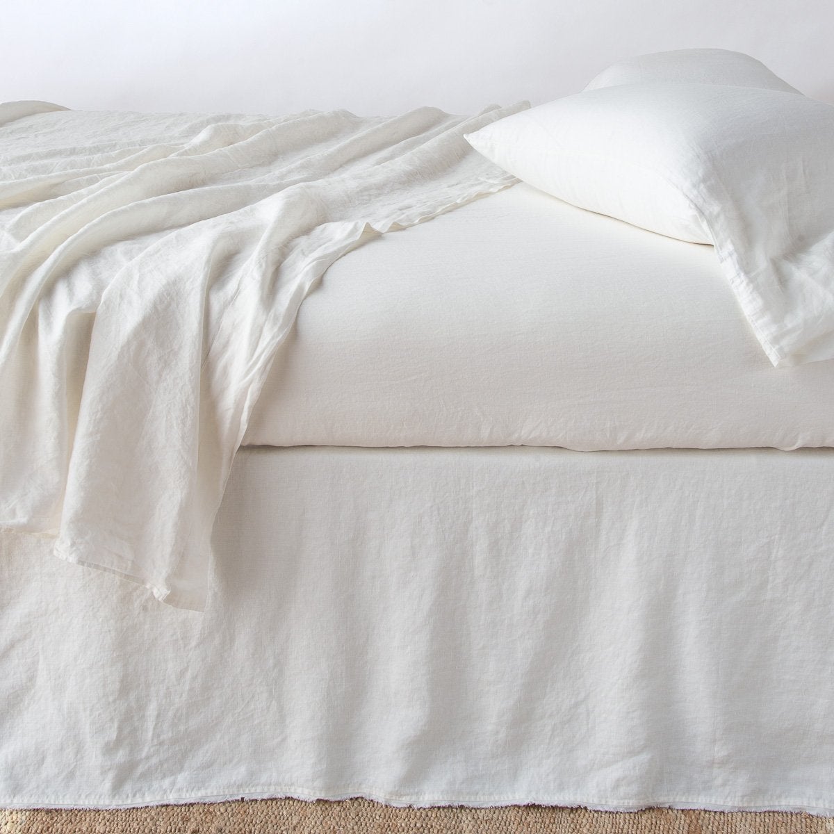 Bella Notte Austin bed skirt in Winter White linen, styled on bed with draped throw and pillow.