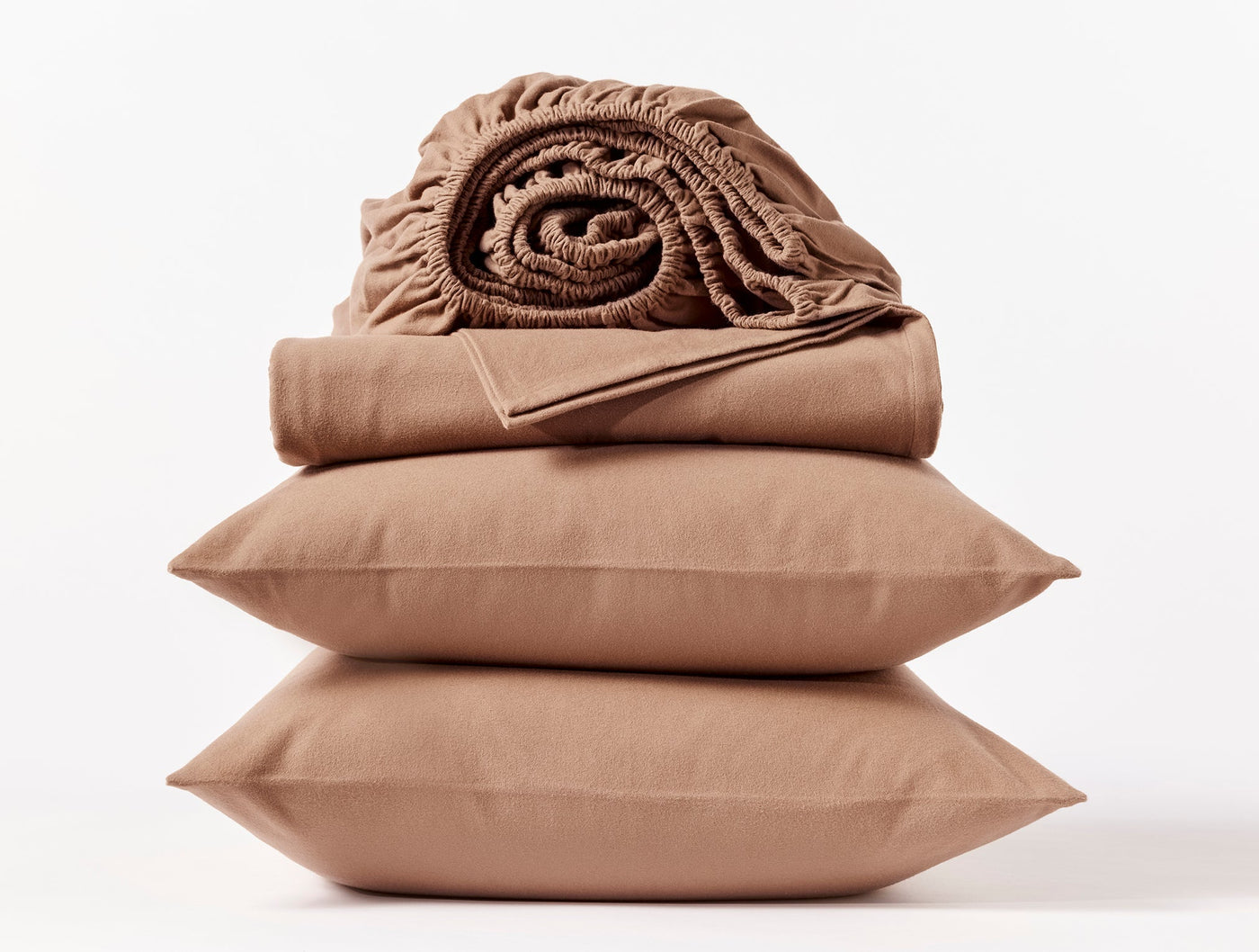 Close-up of stacked caramel Coyuchi flannel pillowcases with folded and rolled sheets on top.
