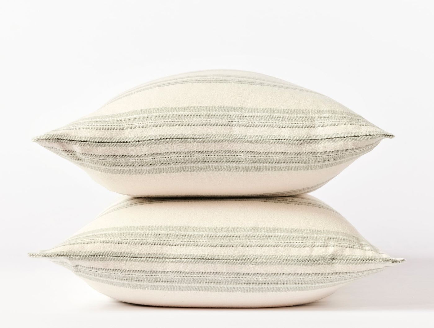 Close-up side view of two stacked Coyuchi flannel pillowcases with sage green horizontal stripes on ivory.