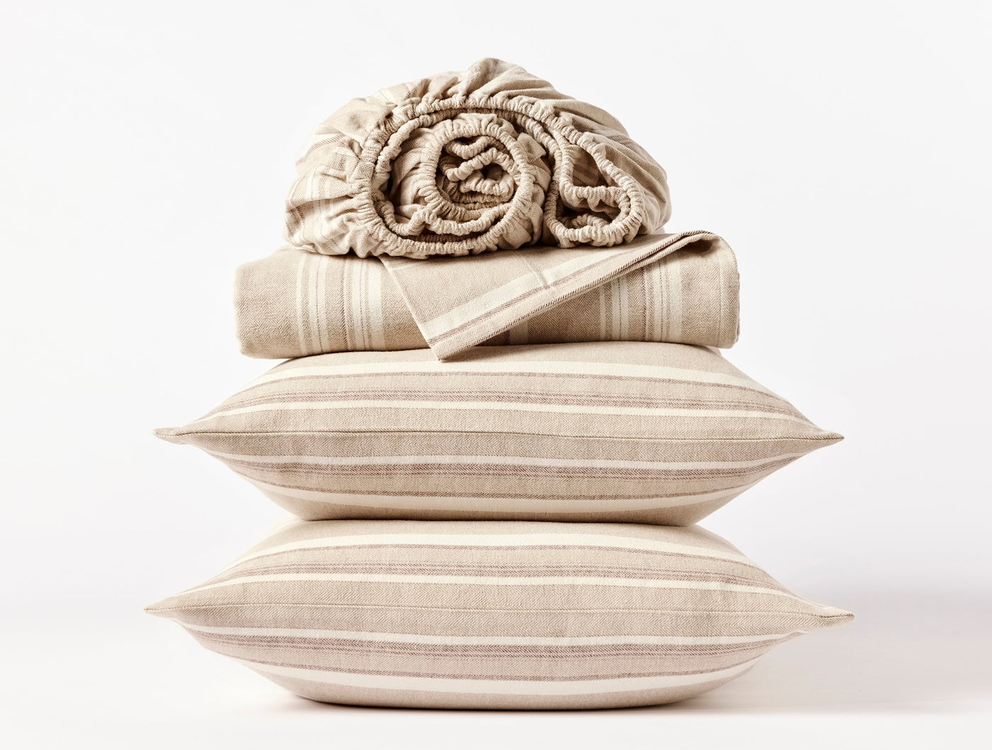 Close-up stack of Coyuchi flannel sheet set with tan stripe pillowcases and rolled fitted sheet.