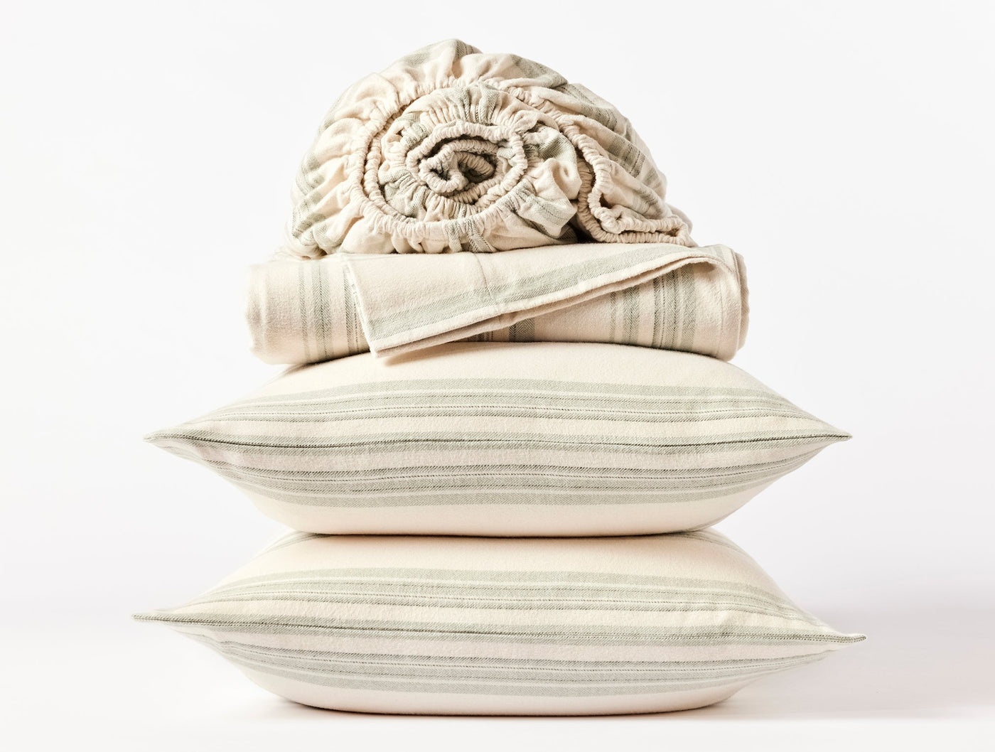 Stacked ivory and sage stripe flannel pillowcases and sheets, with rolled fitted sheet on top.