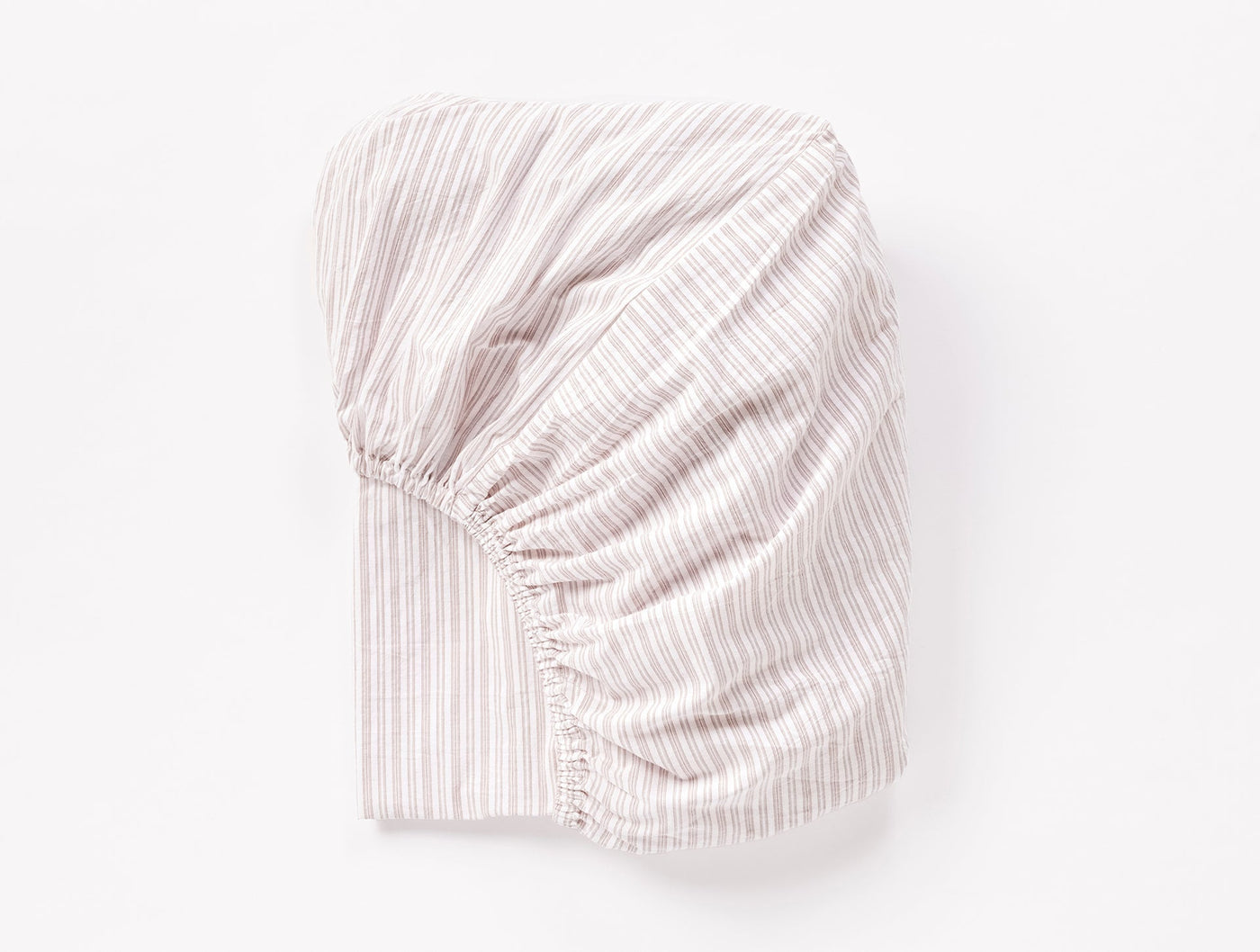 Folded fitted sheet in blush with white pinstripes, elasticized corner visible.