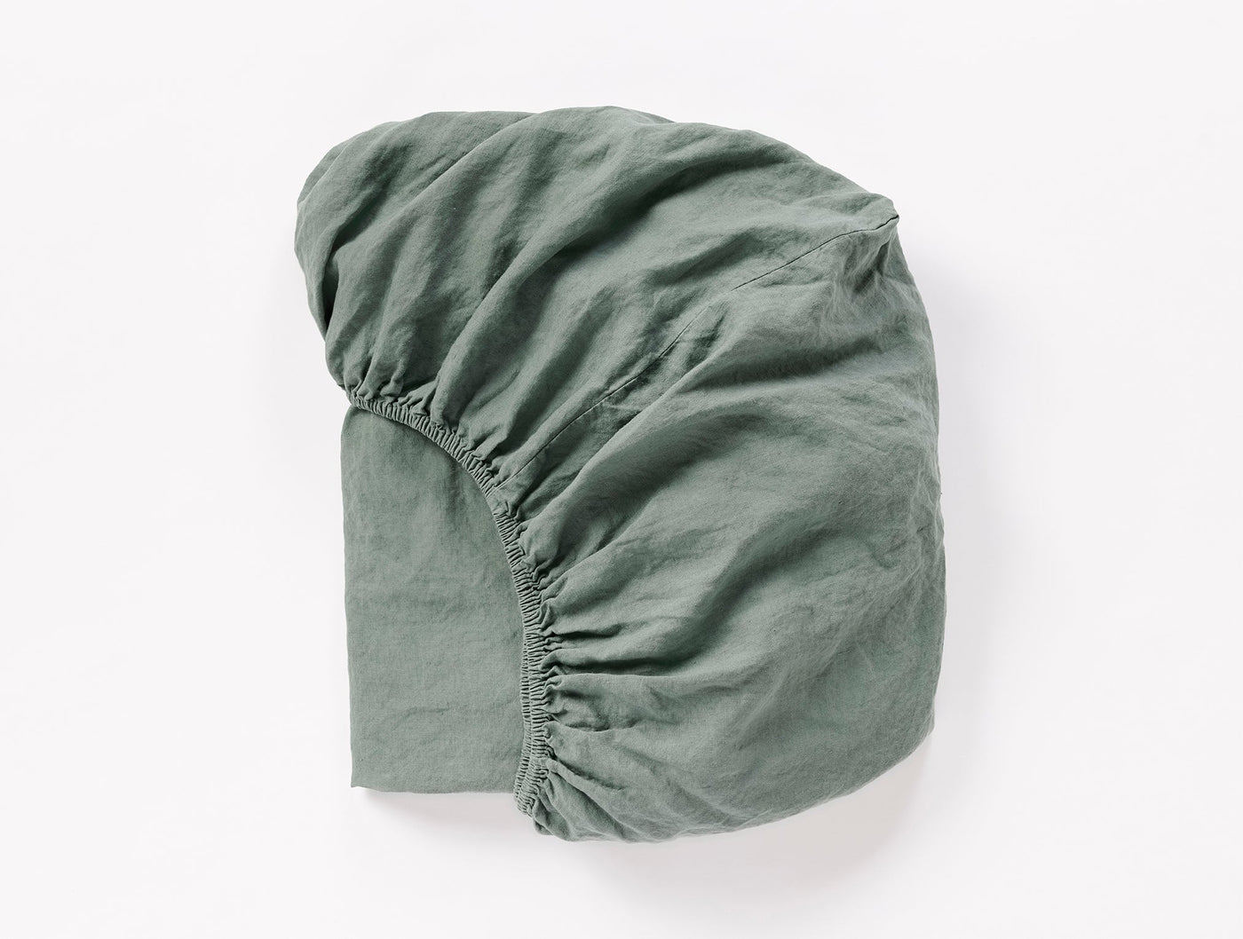 Sage green linen fitted sheet folded to show elasticated corners and relaxed texture.