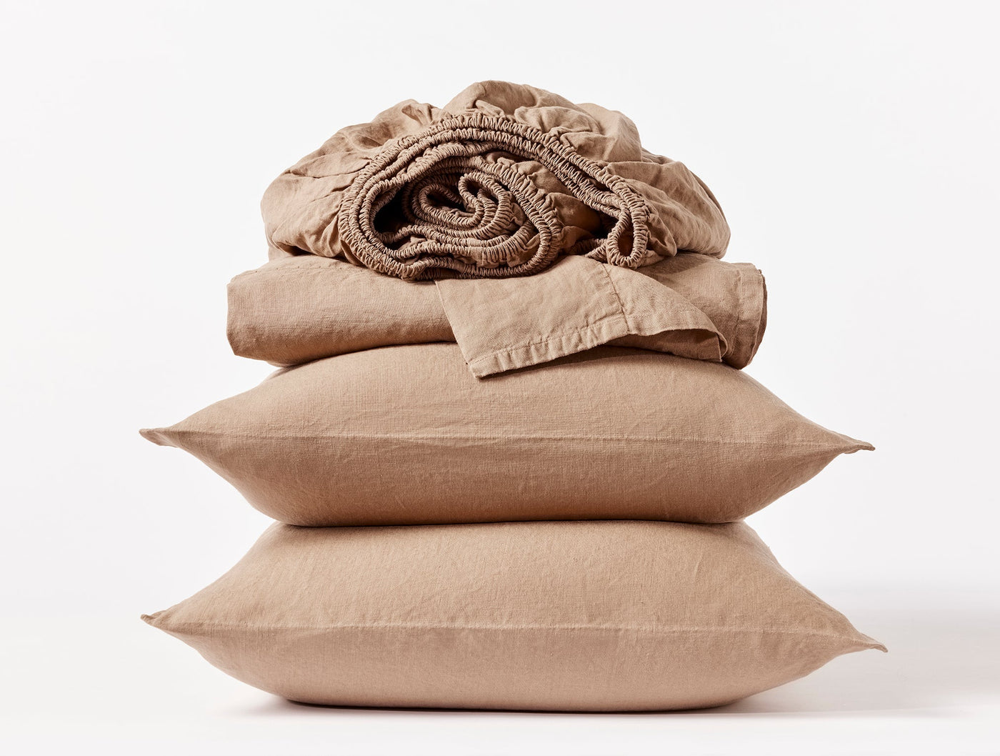 Stacked sand linen pillowcases and folded fitted sheet in relaxed, rumpled texture.