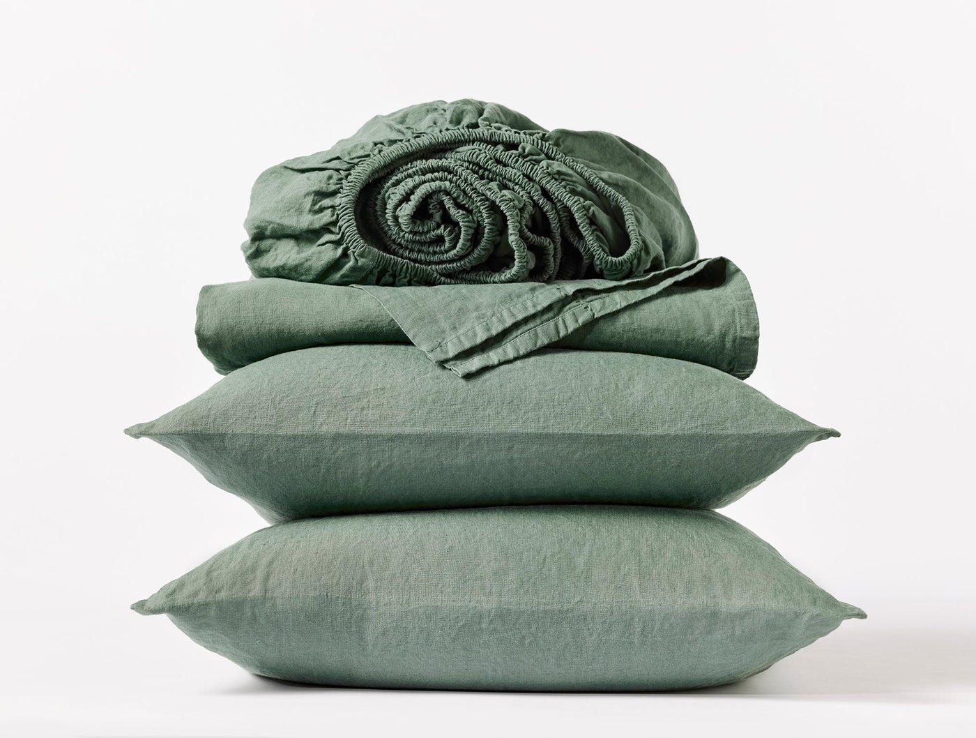 Sage green linen sheet set stacked with pillowcases and rolled fitted sheet.