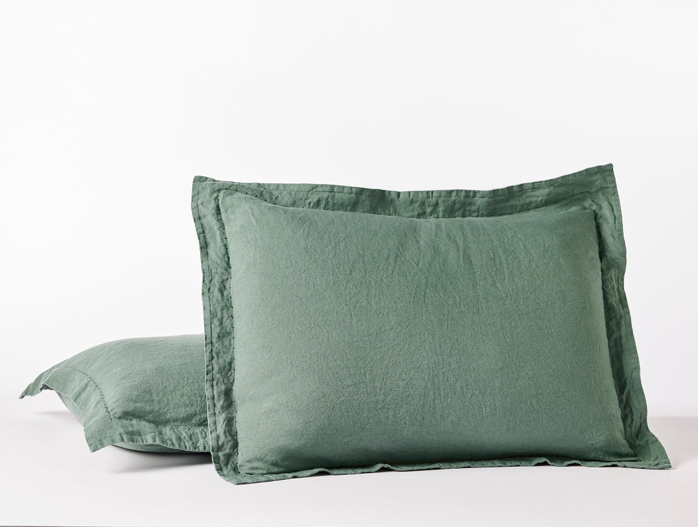 Close-up of two sage green Coyuchi Relaxed Linen pillow shams with flanged edges.