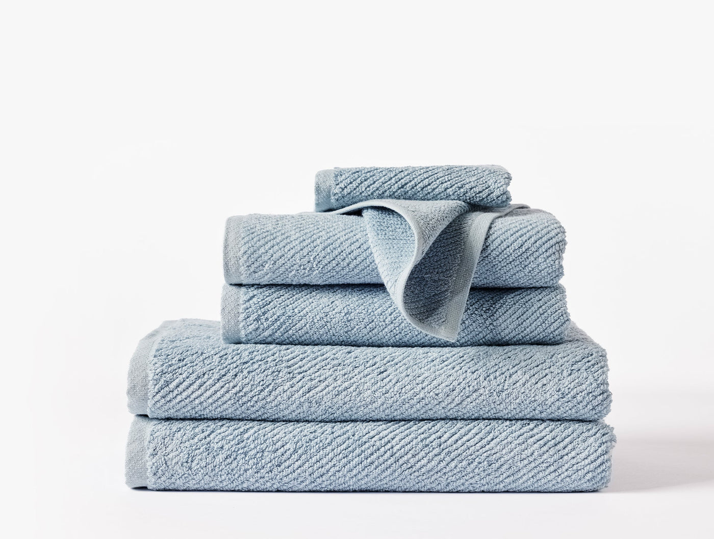 Close-up of stacked Coyuchi Air Weight towels in chambray blue showing ribbed cotton texture.