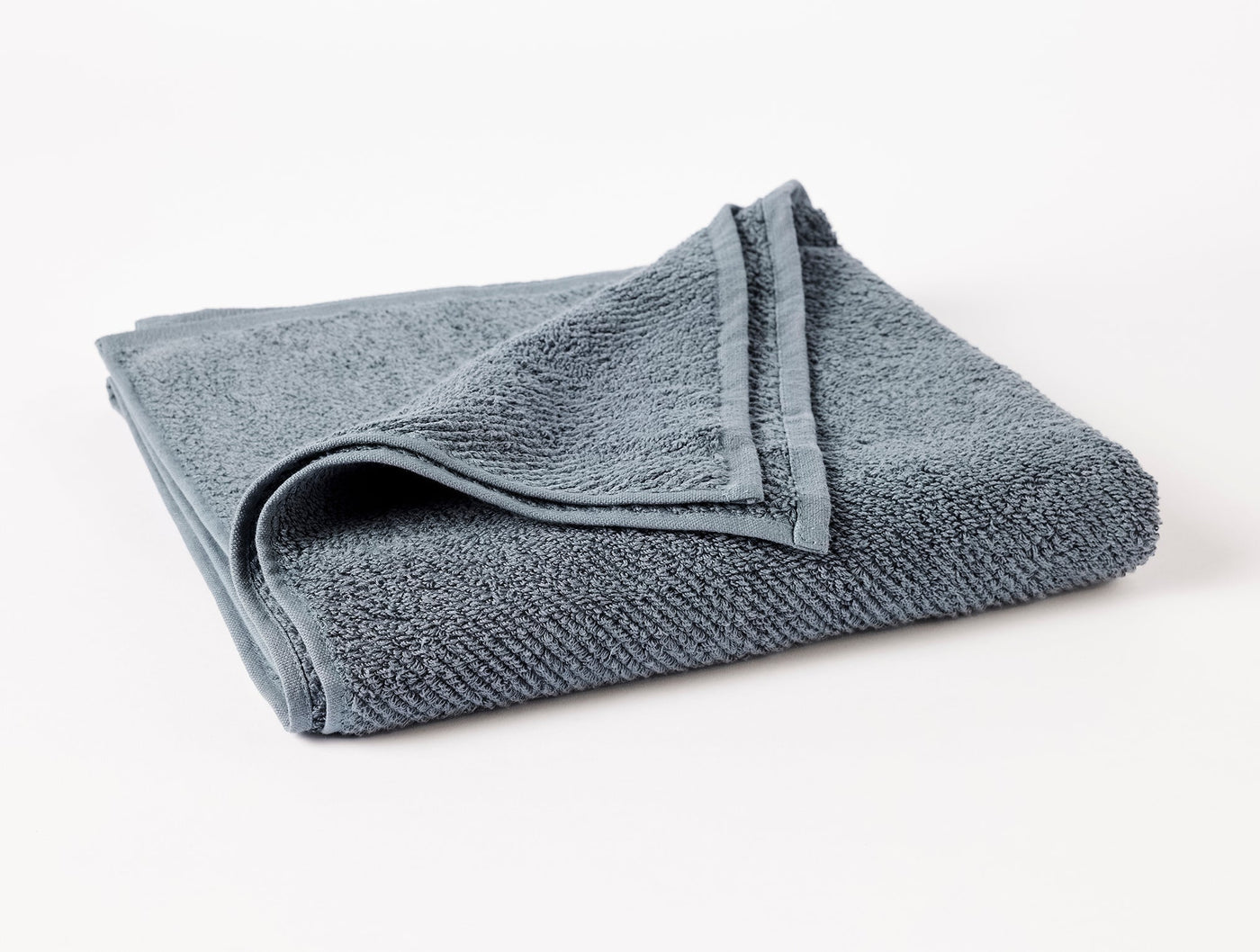 Folded slate blue oversized hand towel showing ribbed texture and hemmed edge detail.
