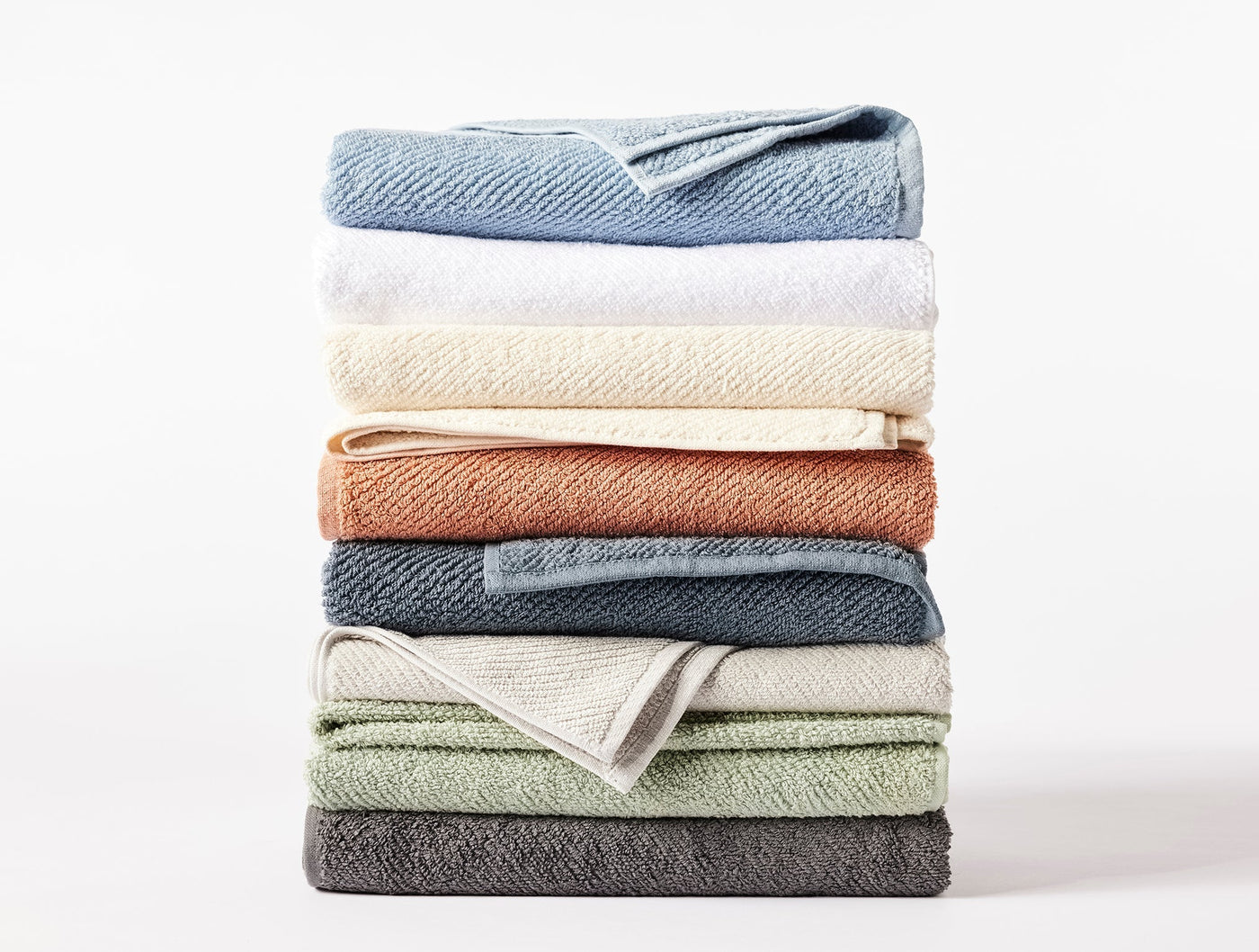 Stack of folded Coyuchi Air Weight bath sheets in eight colorways including sage, slate, and terracotta.
