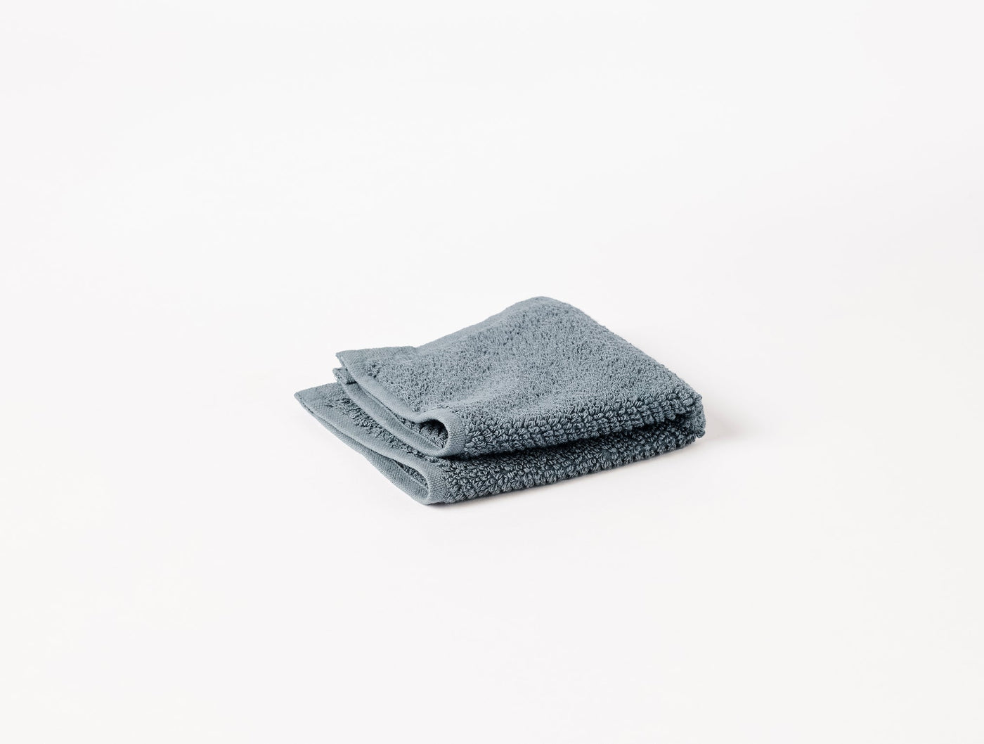 Coyuchi Air Weight washcloth folded flat, slate blue terry cloth, white background.