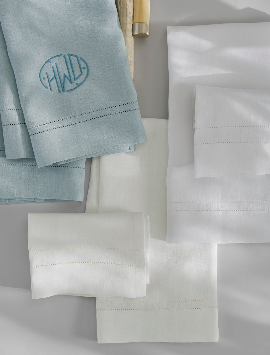 Valentina Hemstitch Guest Towels by Matouk, in elegant blue and white linen, are displayed folded on a flat surface, showcasing embroidered initials and classic hemstitch borders.