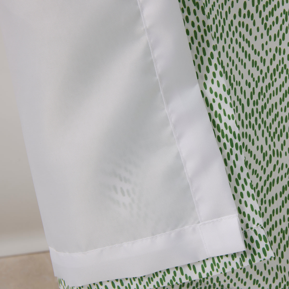 Close-up of a garment with a white water repellent panel inspired by Matouk's Shower Curtain Liner, shown next to green dotted fabric.
