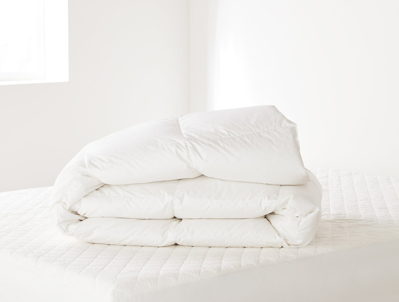 Coyuchi Three Season Down duvet insert folded neatly, white, quilted stitching detail visible.