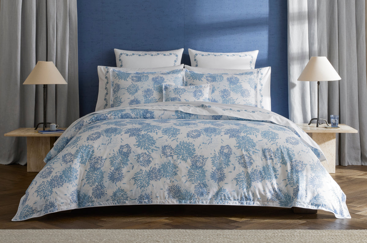 Blue and white chrysanthemum floral duvet styled on a bed with layered pillows.
