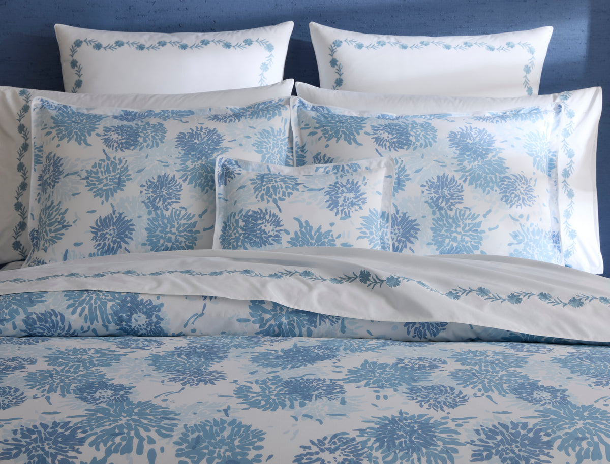 Matouk Chrysanthemum duvet cover in sky blue floral print, layered pillow styling.