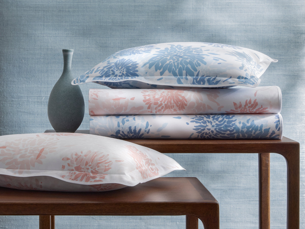 Stacked and loose shams showing blue and blush chrysanthemum print on white cotton.
