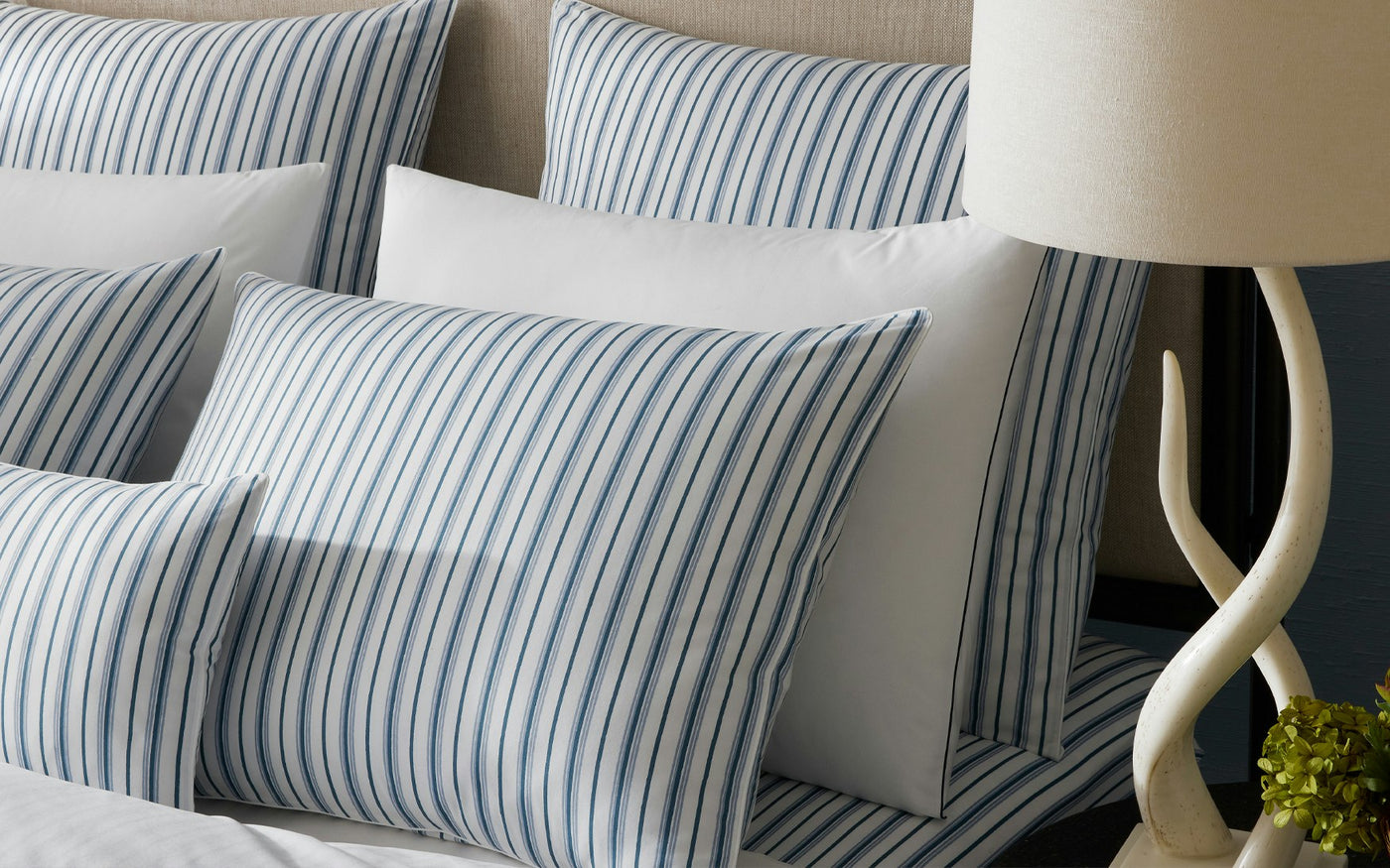 Close-up of Matouk Calypso shams in navy ticking stripe, styled on a made bed with lamp.