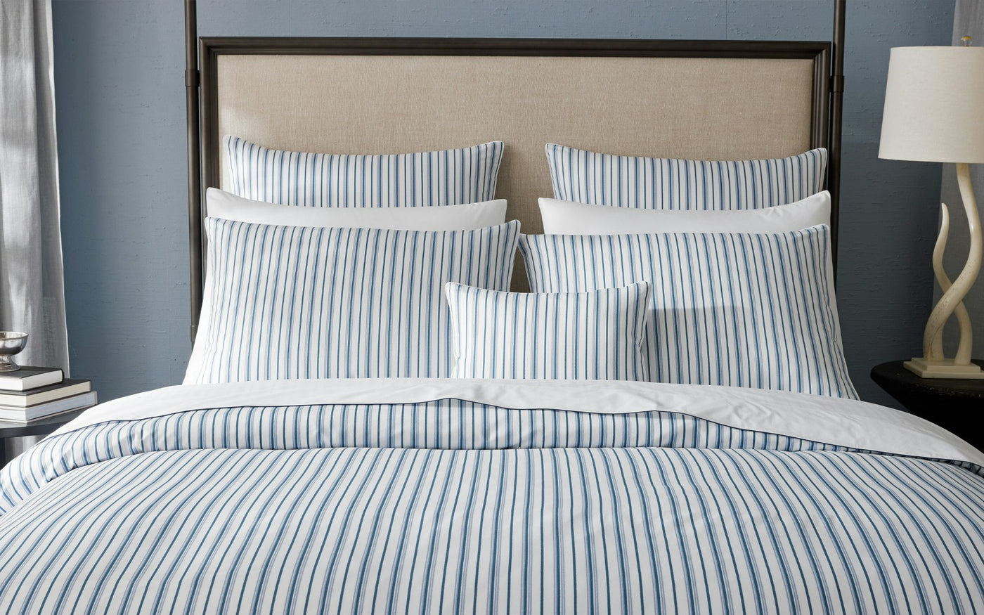 Close-up of Matouk Calypso blue and white stripe bedding styled on a made bed.