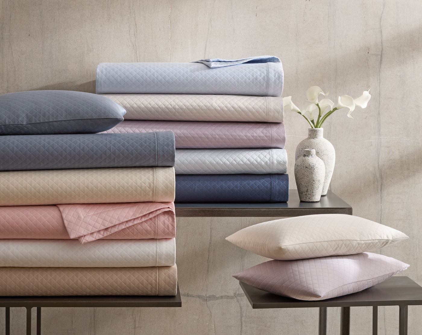 Matouk Petra coverlets folded in multiple colorways including blush, rose, and slate blue.