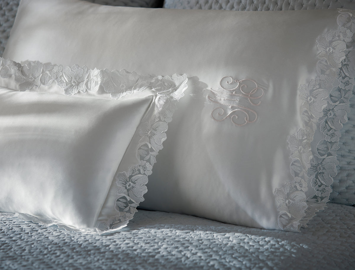 Close-up of Matouk Virginia silk pillowcases in white with floral lace trim detail.