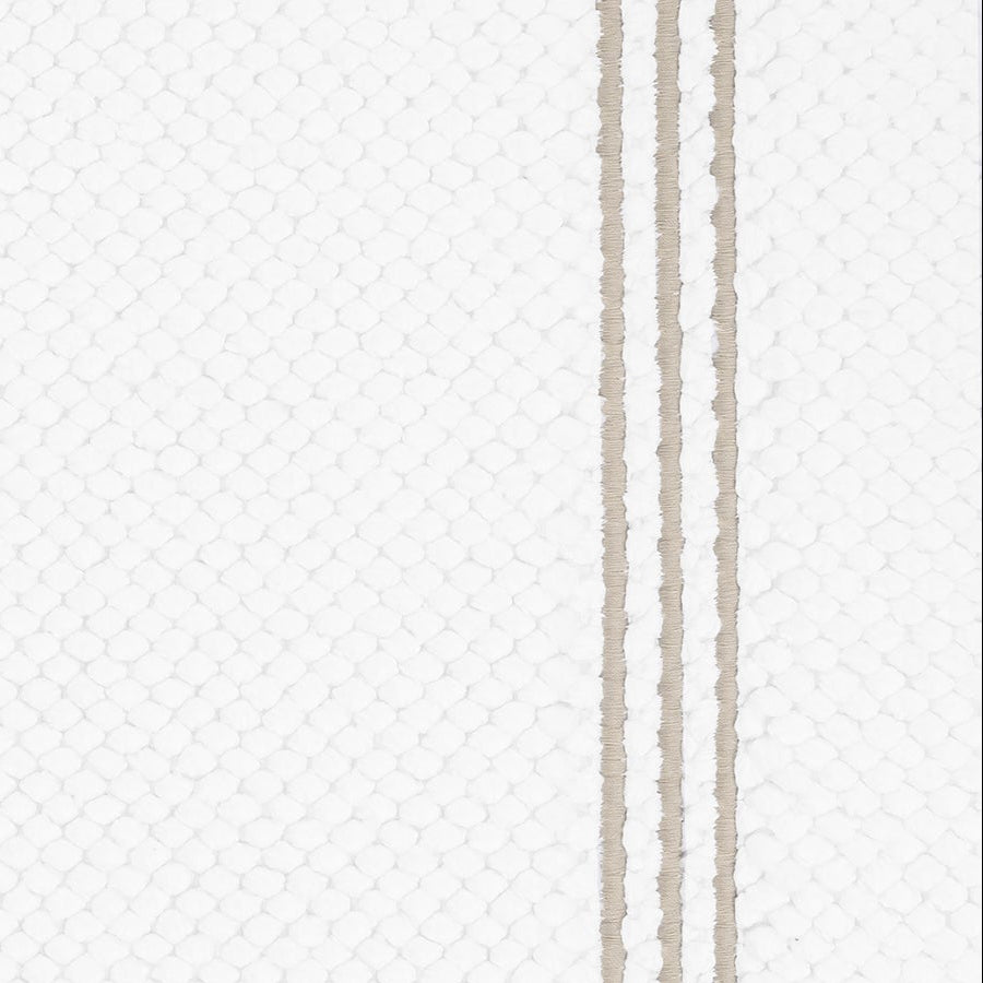 Close-up of white honeycomb-textured bath rug with double taupe stripe border detail.