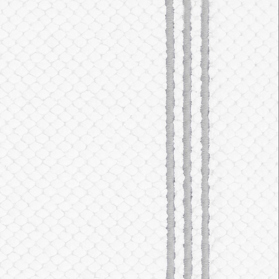 Close-up of white textured bath rug with three silver embroidered border stripes.
