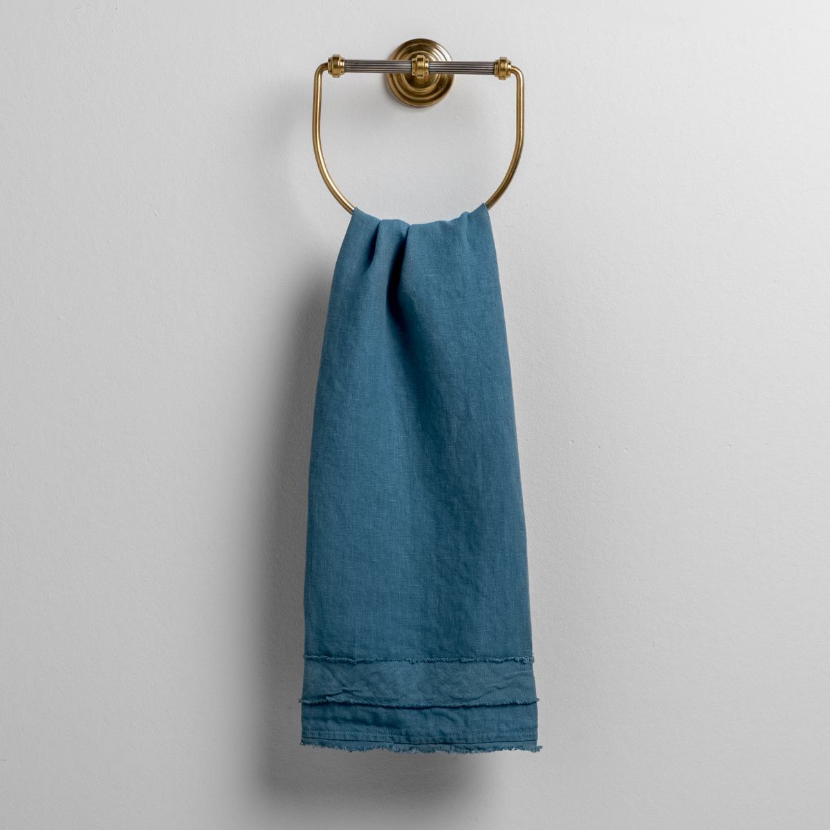 Cenote linen guest towel draped over a brass ring holder, showing hem detail.