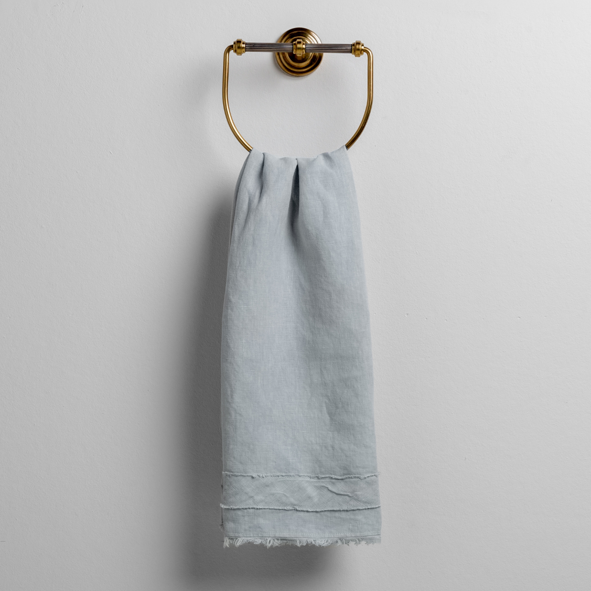 Soft Cloud linen guest towel hanging on a brass ring holder, fringe hem detail visible.