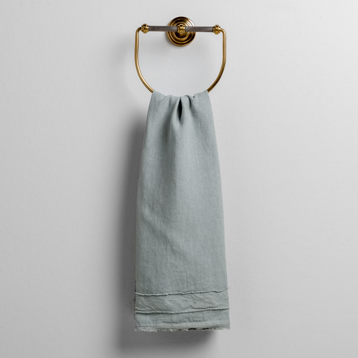 Eucalyptus guest towel draped over brass ring, showing frayed hem detail.