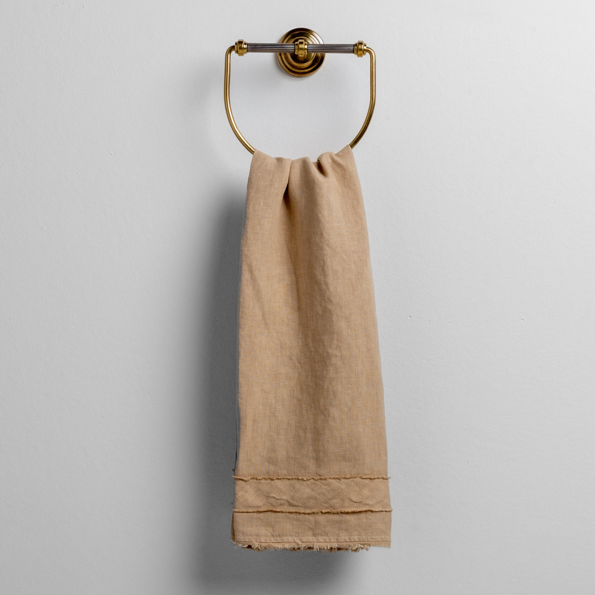 Honeycomb linen guest towel with frayed hem hanging on a brass ring towel holder.