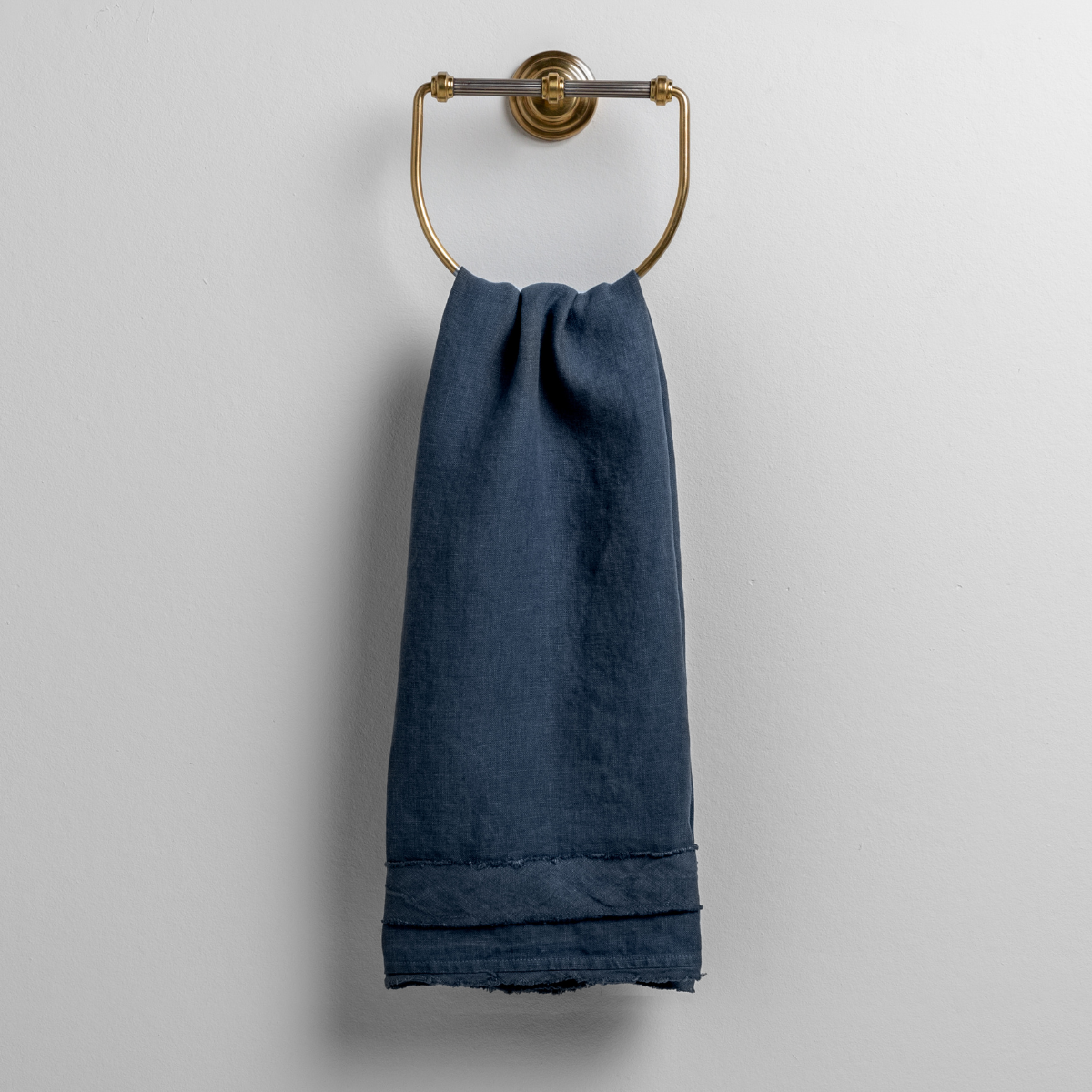 Midnight guest towel draped on brass ring holder, showing hem detail.