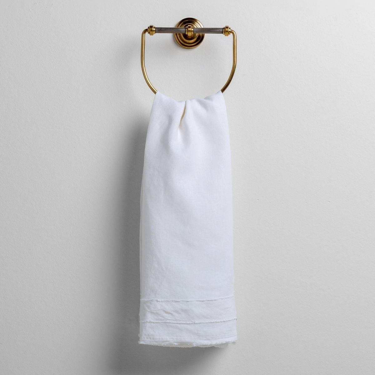Bella Notte Austin guest towel in White, hung on a brass ring, showing hem detail.