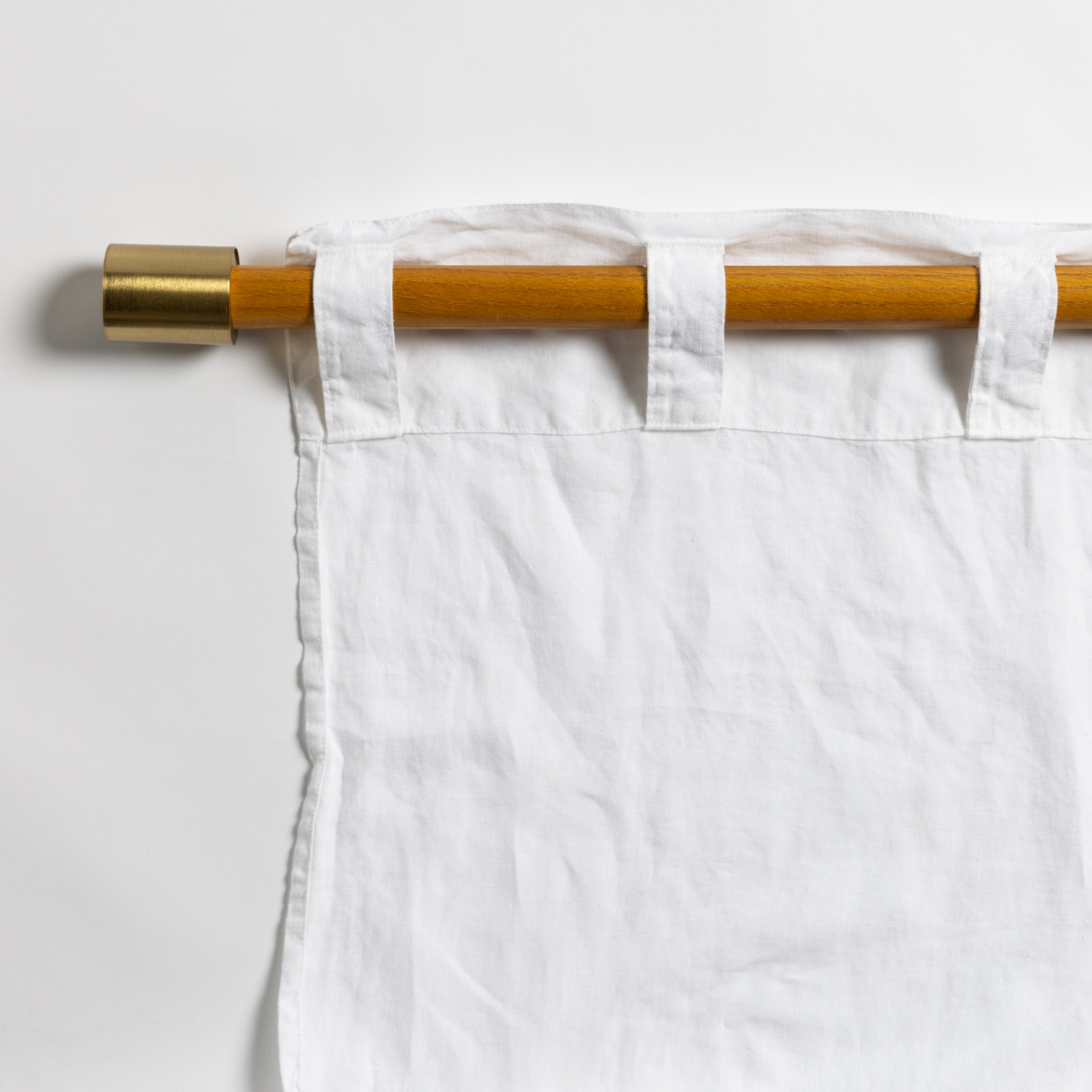Close-up of white linen curtain panel tab tops on a brass-capped wooden rod.